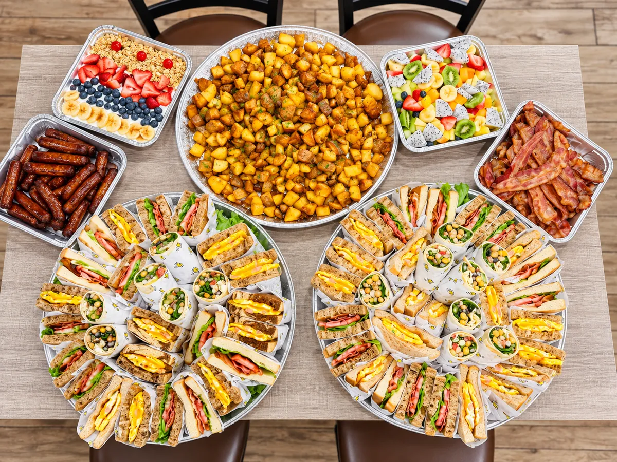 Catering spread: sandwich platters, homefries, bacon, sausage, fruit and waffles